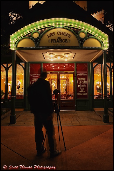 Photographer using a tripod outside the entrance to Les Chefs de France at night in Epcot, Walt Disney World, Orlando, Florida